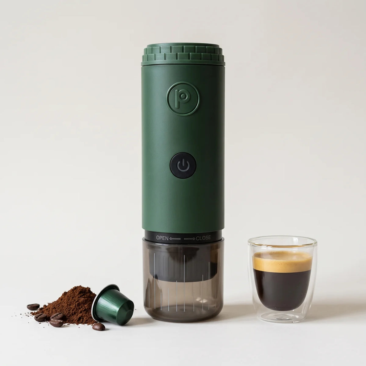 Forest green Origin next to a glass of espresso, ground coffee and a capsule